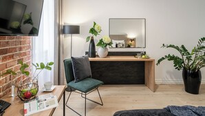 Ein modernes Wohnzimmer mit Fernseher, einem grünen Sessel, einem Holztisch und einer großen Pflanze in einem Topf.