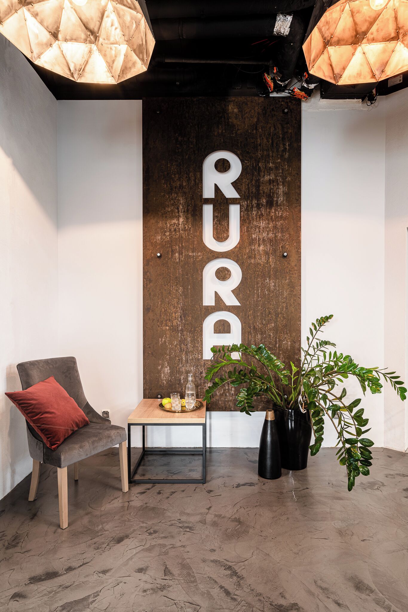 Et moderne værelse med en væg i træ, et lille bord med rød pude, en potteplante og en hængende lampe.