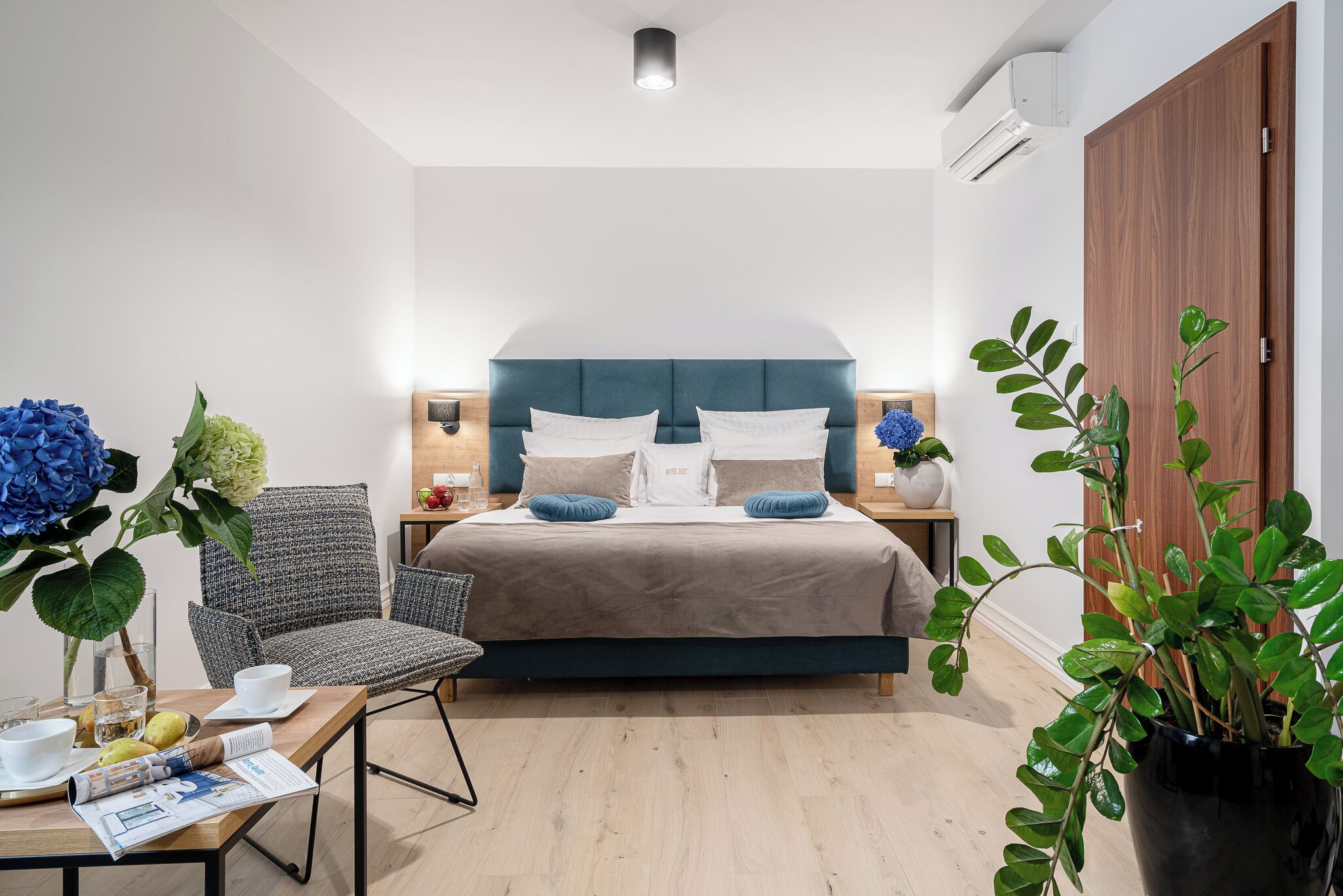 A modern bedroom with a bed, a chair, a table with a vase, and a potted plant.