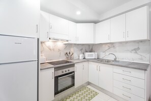 Une cuisine moderne avec des meubles blancs, un four encastré, un four à micro-ondes et un évier.