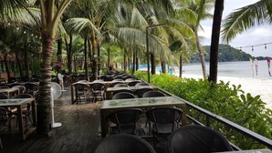 Un restaurant en plein air avec des tables et des chaises en bois, entouré de palmiers et offrant une vue sur la plage.
