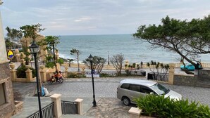 Une rue côtière bordée d’une voiture garée, d’une moto et d’un chemin piétonnier menant à la plage.