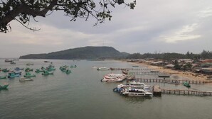 Une zone côtière où de nombreux bateaux sont amarrés à des quais, avec une plage de sable et une colline en arrière-plan.