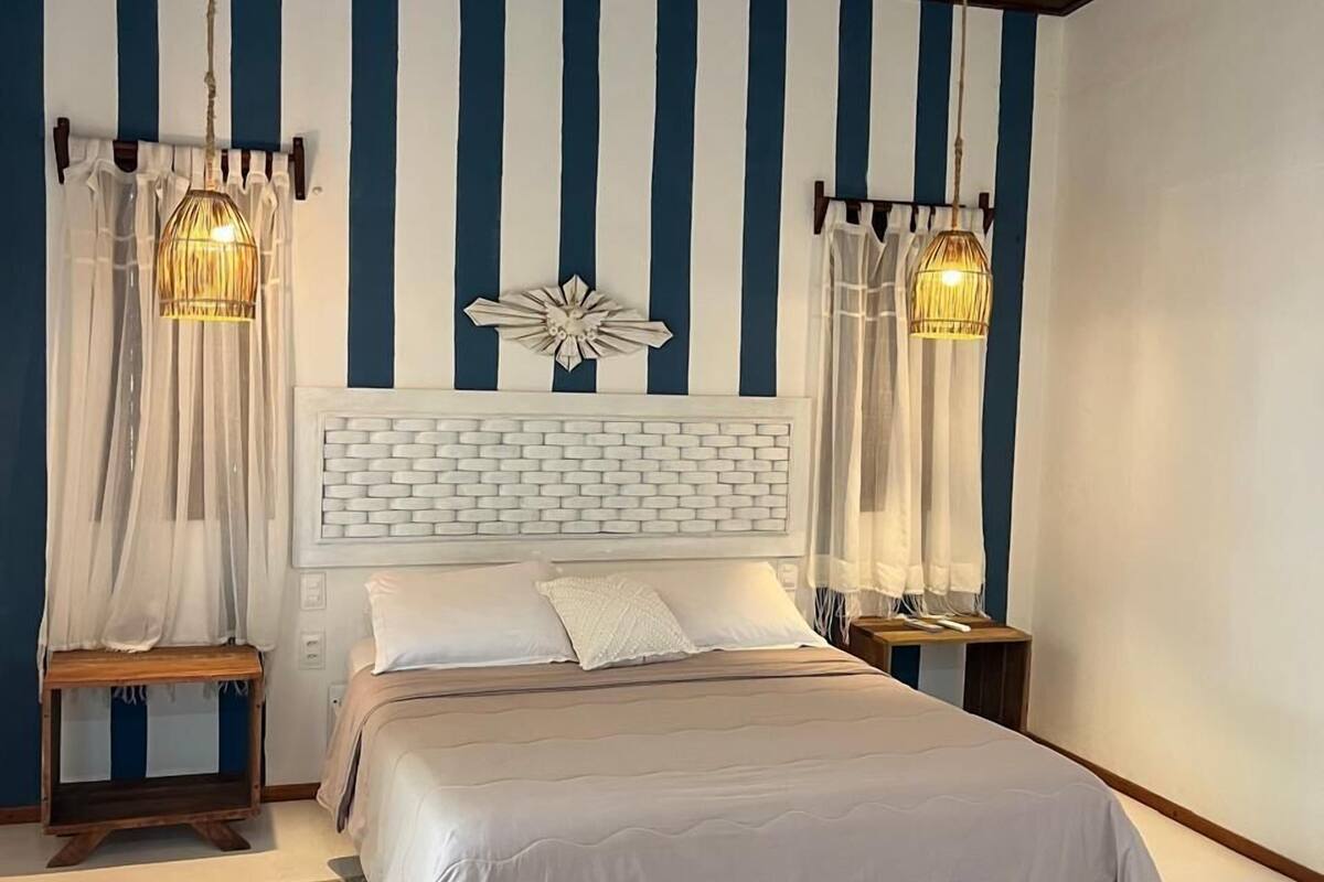 A bedroom with a striped wall, a white headboard, and two bedside lamps.