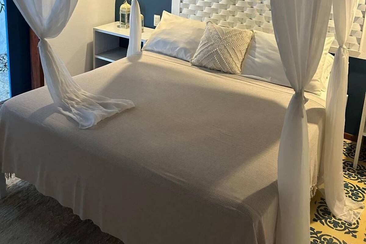 A bed with white bedding and a canopy, a bedside table with a lamp, and a nightstand with a lamp.