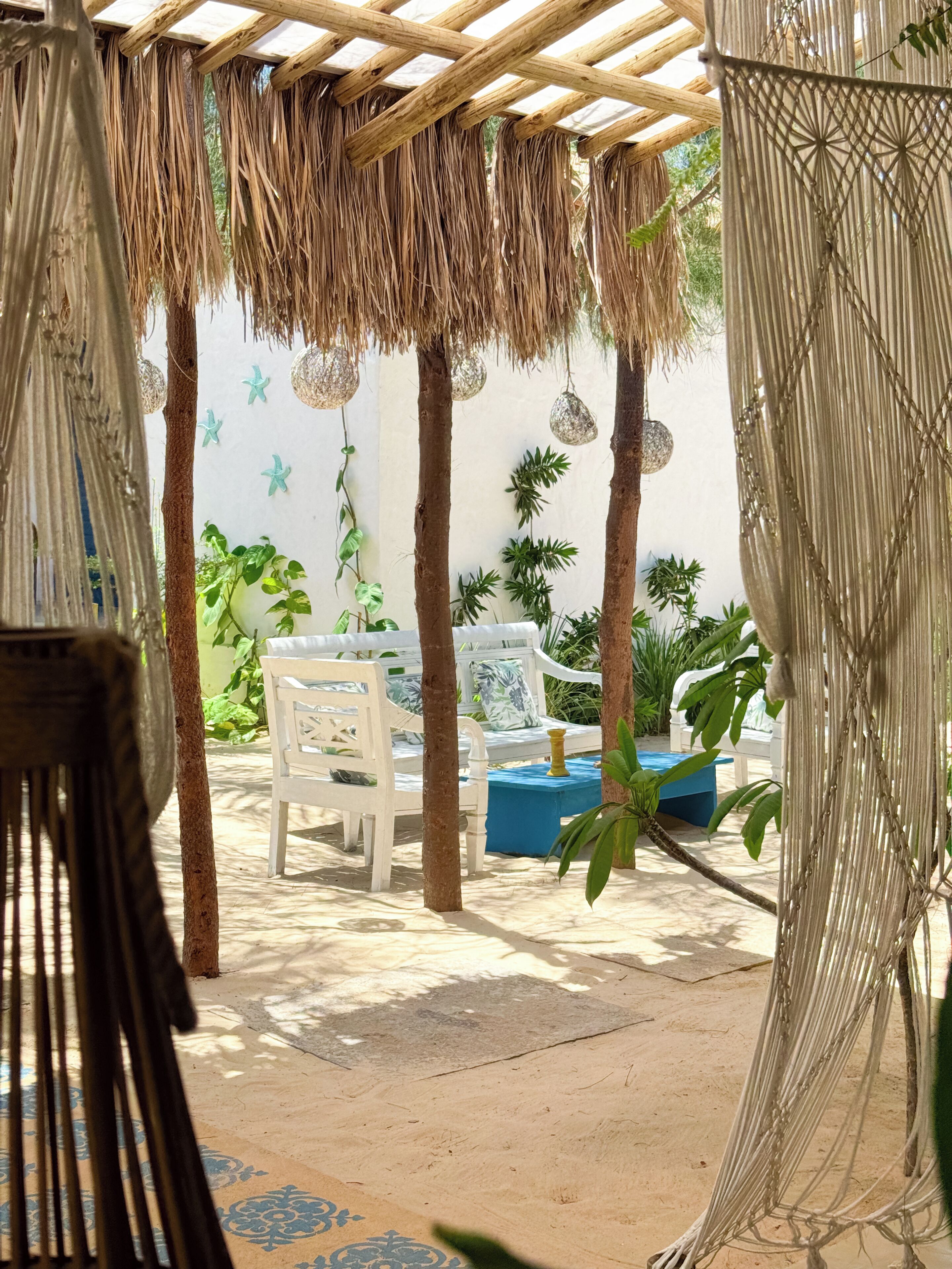 A covered outdoor seating area with a white bench, a blue table, and hanging starfish decorations.