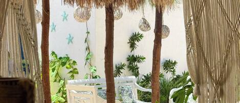 A covered outdoor seating area with a white bench, a blue table, and hanging starfish decorations.