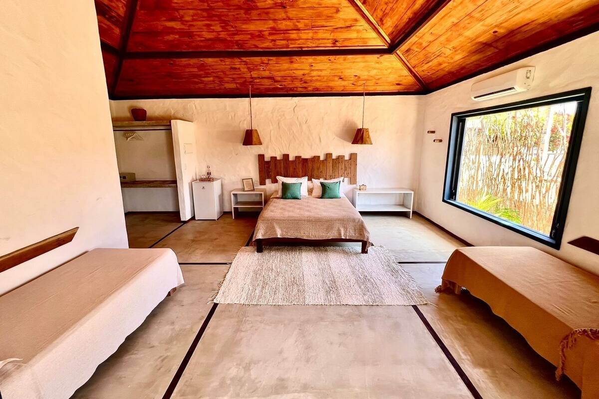 A bedroom with a large bed, two bedside tables, a wooden headboard, a large window, and a ceiling fan.
