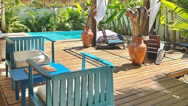 A wooden deck with blue chairs and a table, a pool, and a thatched roof structure. - Pousada La Vida Boutique (Amontada)