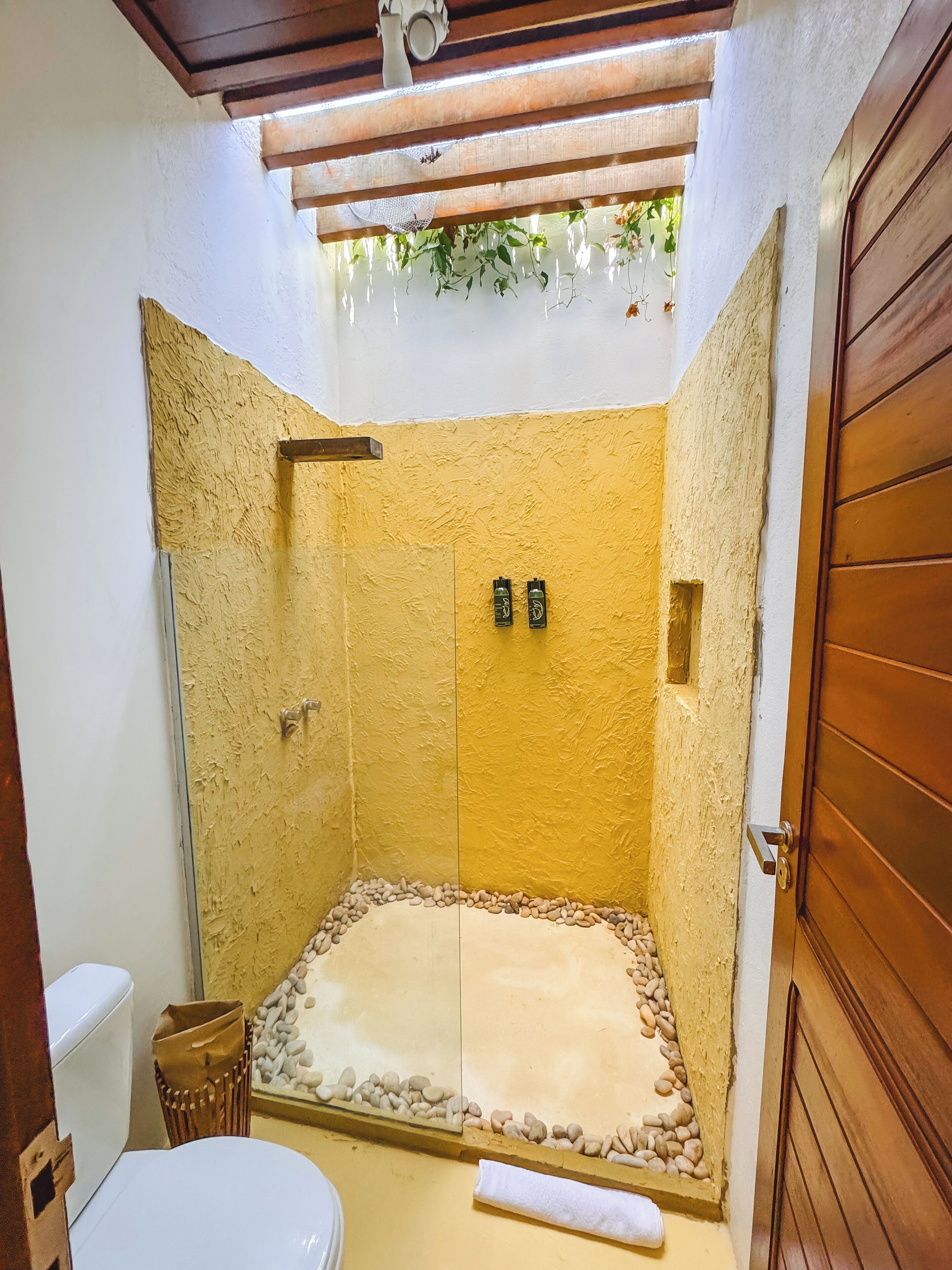 Un espacio de ducha pequeño y cerrado, con una pared amarilla con textura, una puerta de madera y un inodoro blanco.