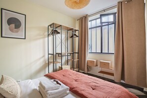Un dormitorio con cama, armario, ventana con cortinas y un cuadro en la pared.