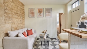 Un salon moderne avec un mur en pierre, un canapé avec des coussins, une table basse avec un vase et un coin repas avec une table et des chaises en bois.