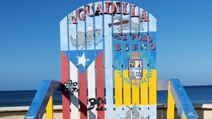 A colorful beach chair with a sign that reads "AGUADILLA SE PUSO BUENO" and features a shark and a coat of arms.