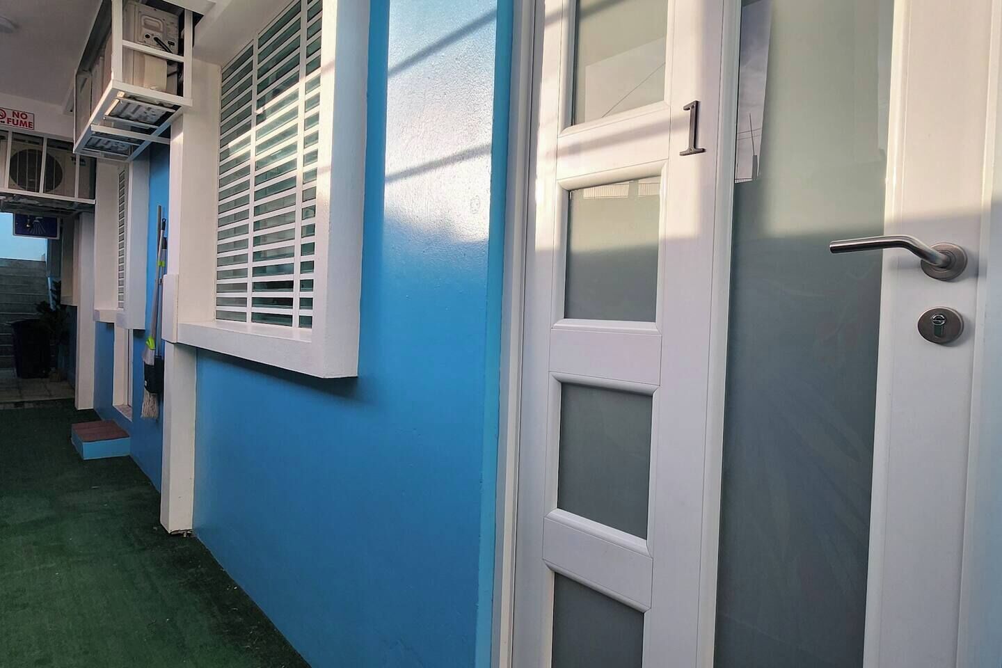 Un pasillo con pared azul, una puerta blanca con panel de vidrio y una ventana con contraventanas blancas.