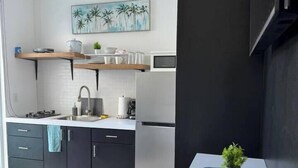 A modern kitchen with dark cabinets, a white countertop, and a microwave. There is a painting of palm trees on the wall above the counter. - Sweet Sunset 4 Playa Rompeolas, Aguadilla (Aguadilla Pueblo)