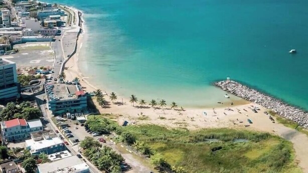 Oversigtsbillede af et kystområde med strand, bygninger og et klart, blåt hav.