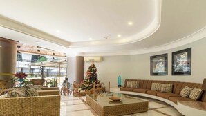 A spacious living area with a curved ceiling, a large sofa set, a Christmas tree, and a view of the outside balcony. - Apto no Guarujá com Piscina a Passos da Praia (Guarujá)