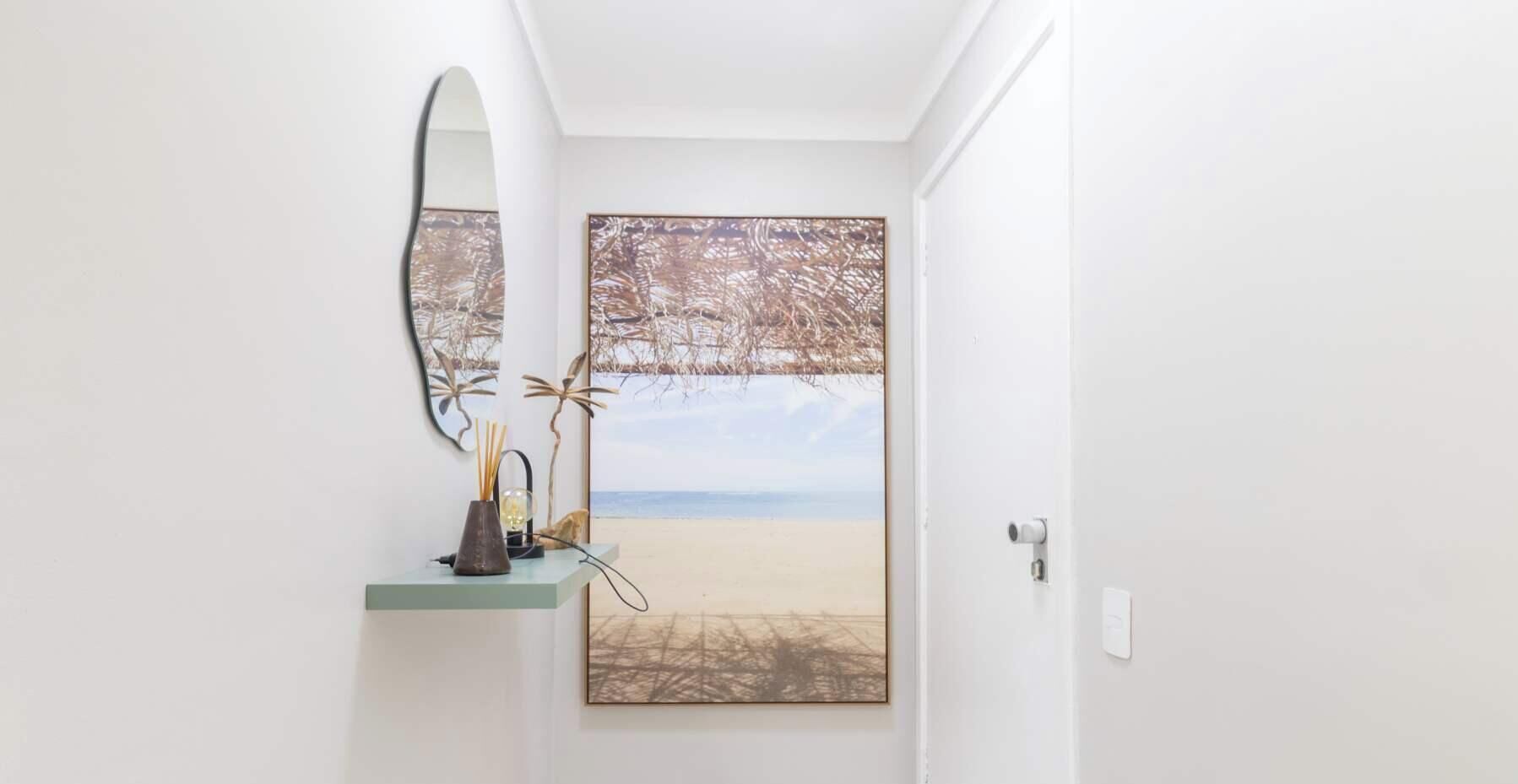Een gang met een grote spiegel, een afgebeeld strandgezicht en een klein schapje met decoratieve objecten.