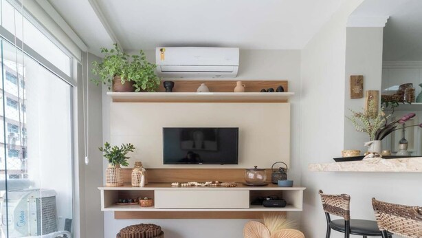 A modern living room with a flat-screen TV mounted on a wooden shelf, surrounded by decorative items and plants. - Apto no Guarujá com Piscina a Passos da Praia (Guarujá)