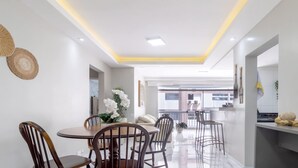A modern kitchen with white cabinets, a wooden dining table, and chairs. There is a balcony with a view of the city. - Apto no Guarujá com Piscina a Passos da Praia (Guarujá)