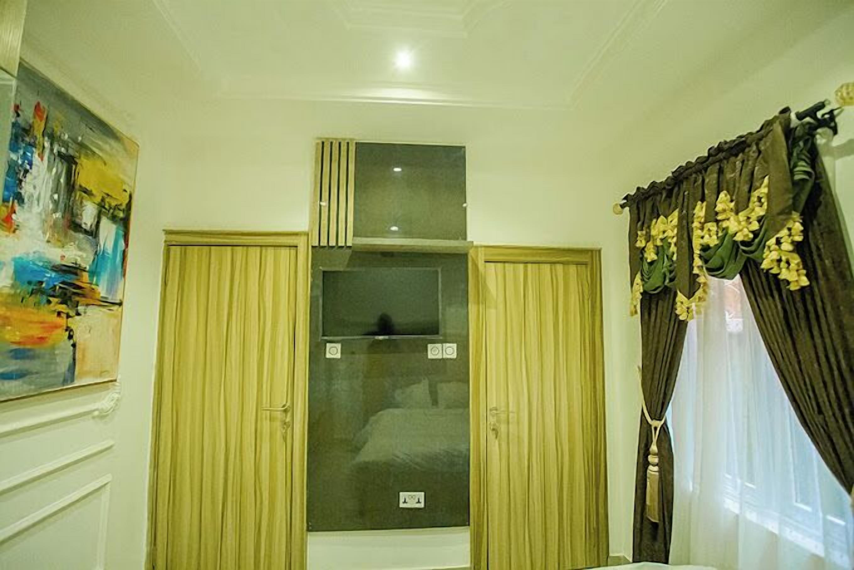 Una camera d'albergo con un grande quadro appeso al muro, un armadio con specchio e una finestra con tende.