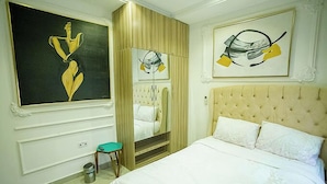 Un dormitorio con una cama grande, una silla, una mesita y dos cuadros en la pared.