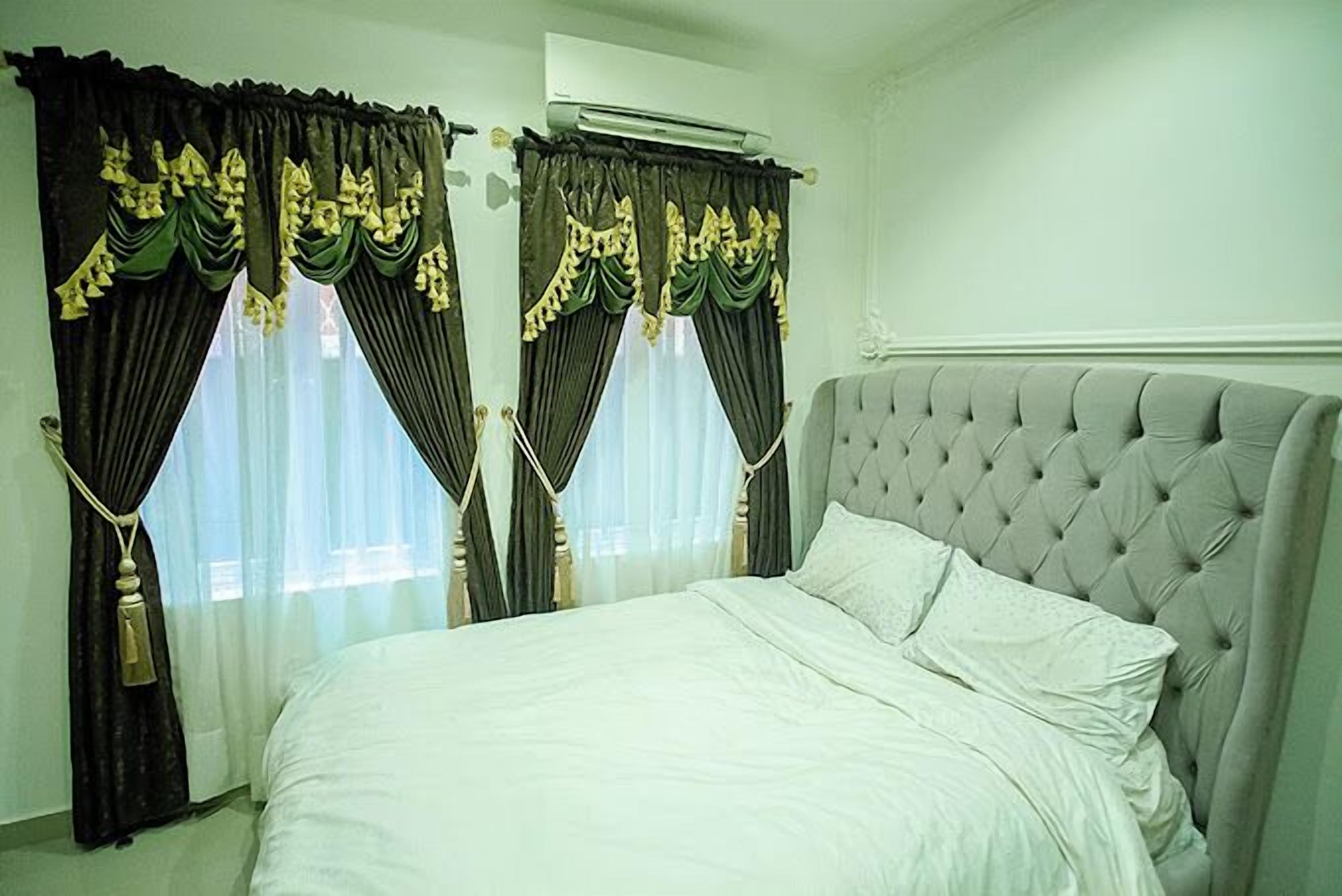A bedroom with a tufted headboard, a bed with white linens, and curtains with gold trim.
