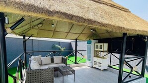 Un espacio de estar techado al aire libre con techo de paja, un sofá y una mesita.