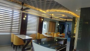 A modern dining area with a glass-top table, yellow chairs, and ceiling fans. - SOLITUDE (Dharamshala)