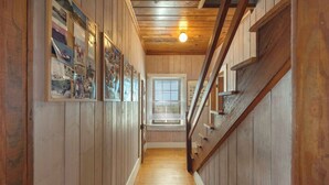 Un pasillo interior de madera con una escalera, paredes de madera y una ventana con persianas.
