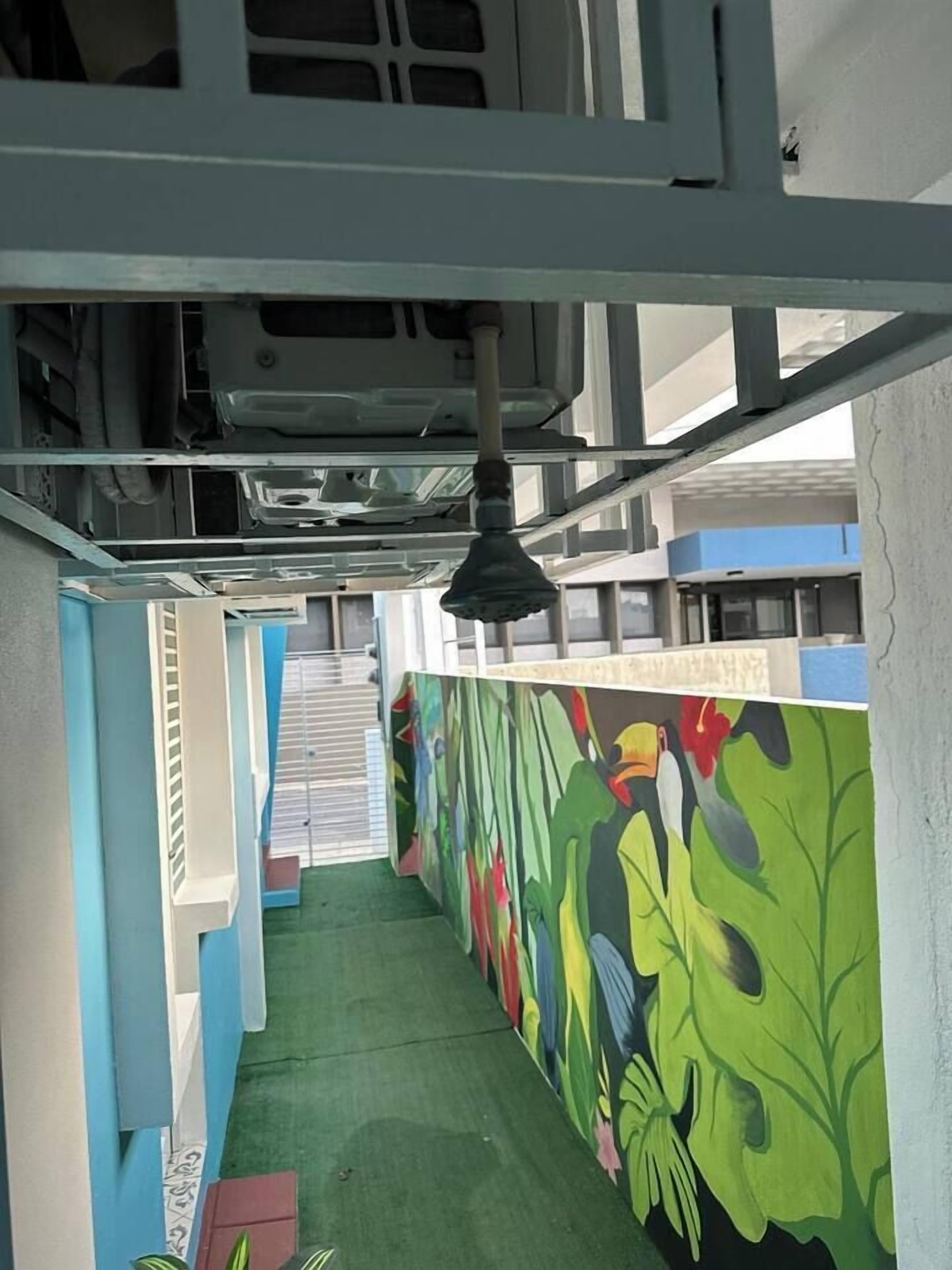 A narrow hallway with a green carpet, a colorful mural on the right wall, and a ceiling with exposed ductwork.