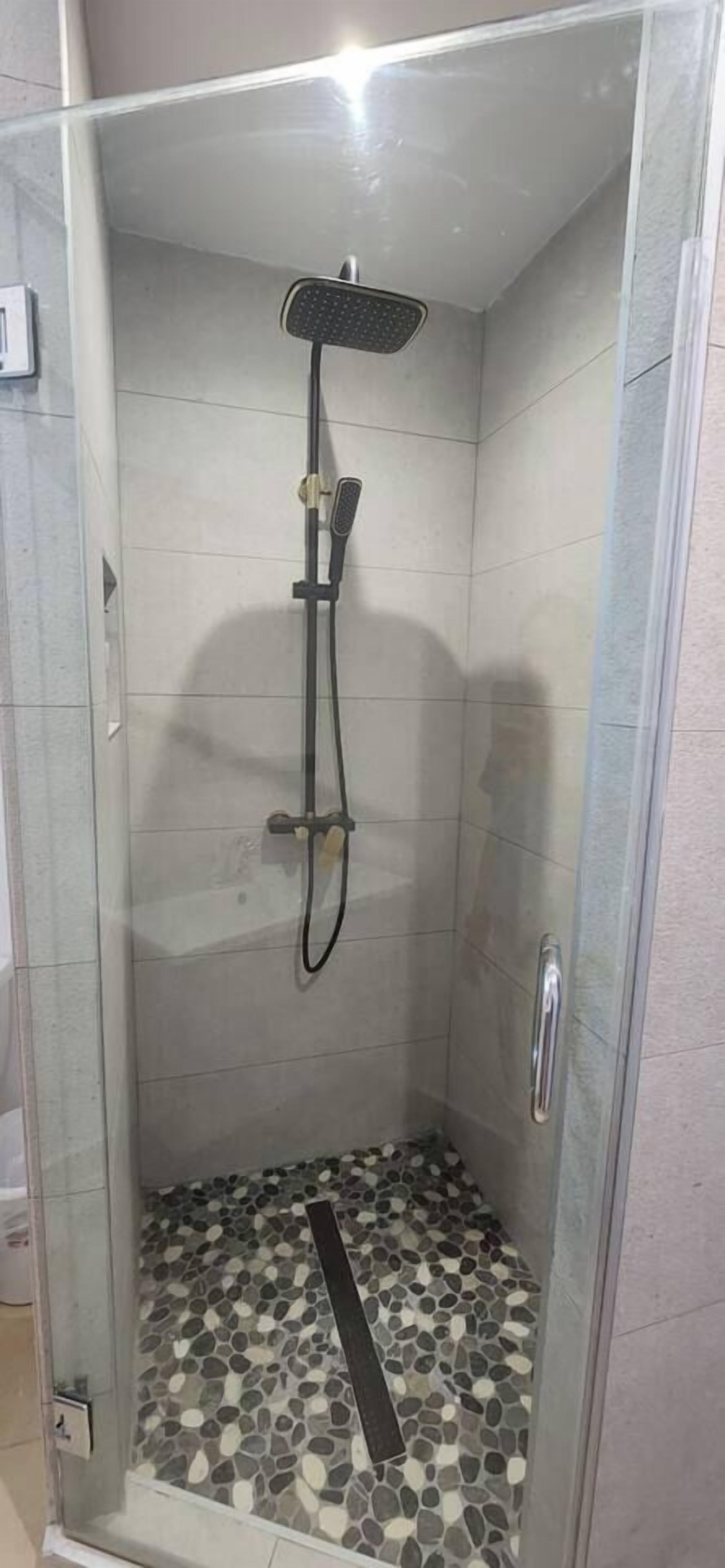 A glass-enclosed shower with a tiled floor and a handheld showerhead.