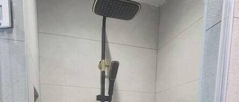 A glass-enclosed shower with a tiled floor and a handheld showerhead.
