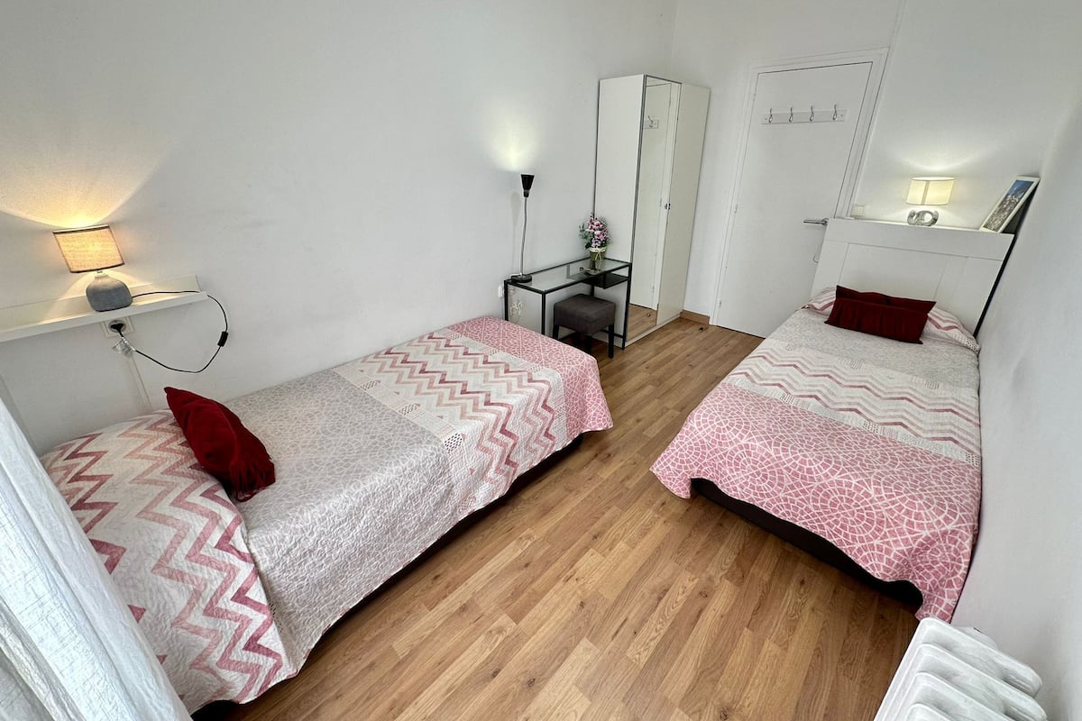 A bedroom with two single beds, a desk, a wardrobe, and a mirror.