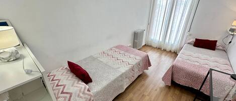 Una habitación pequeña y bien iluminada con dos camas, un escritorio y un radiador.