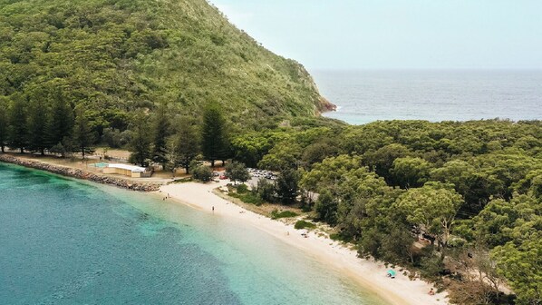 Vista aérea de una zona costera con playa, bosque frondoso y una vista despejada del mar.