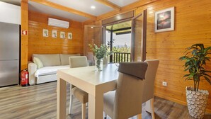 Ein Interieur einer Holzhütte mit Esstisch, Stühlen, einer Couch, einem Feuerlöscher und einer Topfpflanze.