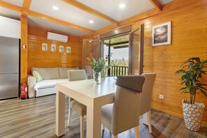 A wooden cabin interior with a dining table, chairs, a sofa, a fire extinguisher, and a potted plant.