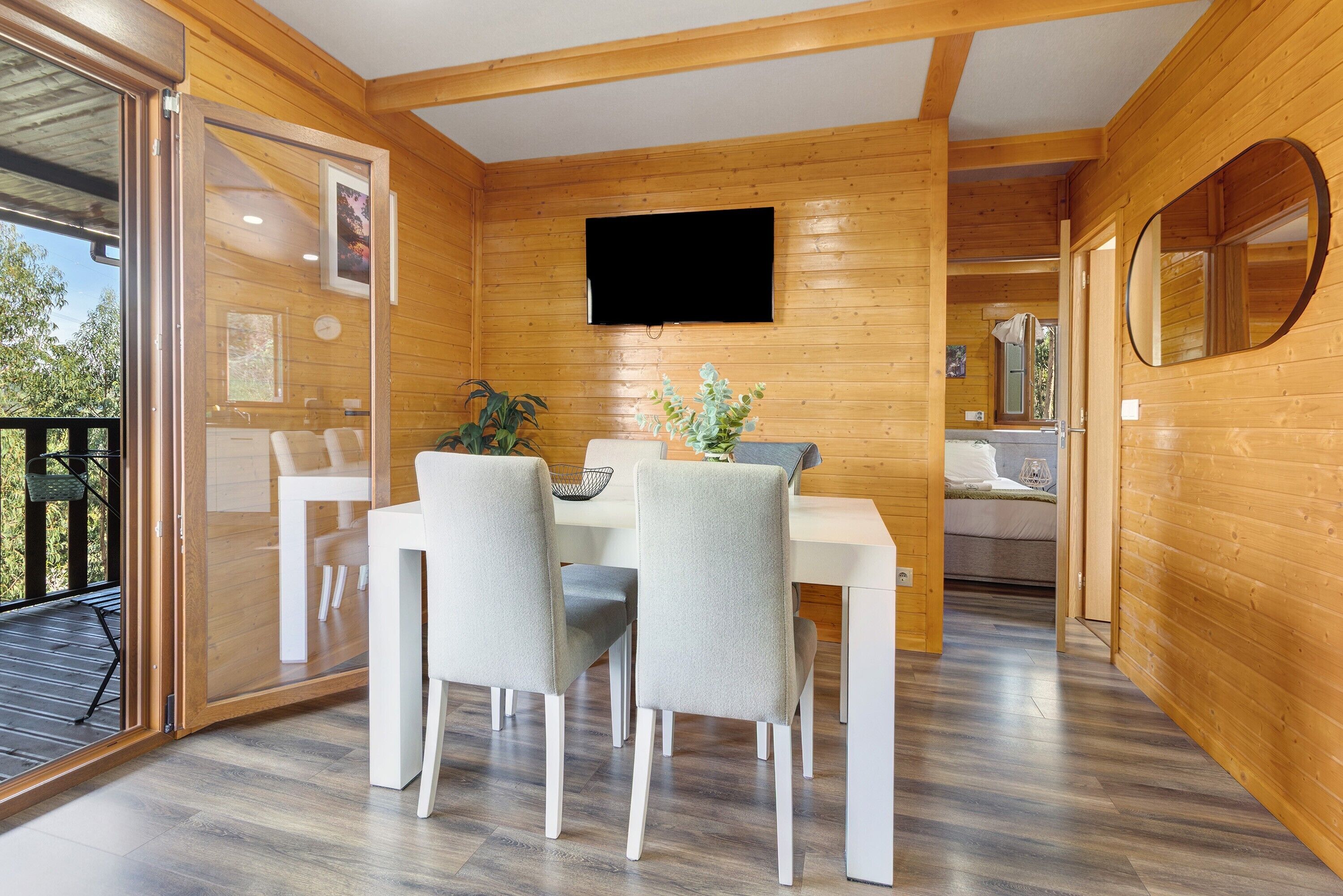 Ein Holzinterieur mit Essbereich, einem an der Wand befestigten Fernseher und einer Glastür zum Außenbereich.