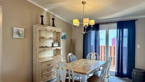 Un coin repas avec une table en bois et des chaises blanches, un buffet blanc avec des étagères et un lustre.