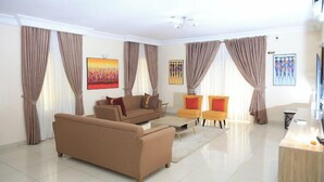 A modern living room with a beige sofa, two armchairs, a coffee table, and a TV stand. - Apartment 1010 (Abuja)