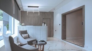 A modern reception area with a white counter, two grey sofas, a marble floor, and a large window. - Apartment 1010 (Abuja)
