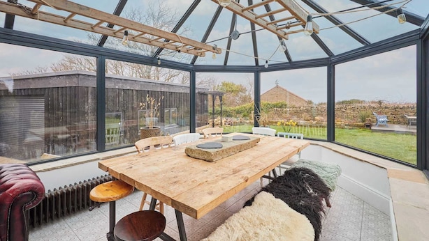 Un invernadero con una mesa y sillas de madera, un radiador y vistas al jardín.
