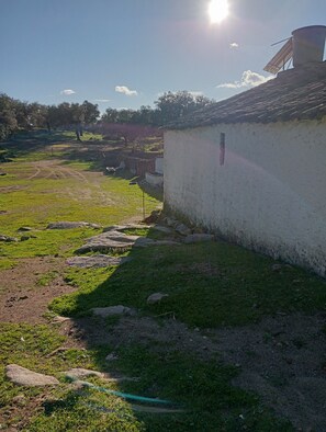 Paisaje rural con una edificación blanca, cielo despejado y un camino iluminado por el sol.