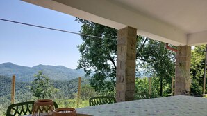Une table recouverte d’une nappe à motifs floraux, deux bougeoirs orange et un plateau en marbre. L’ensemble est agrémenté d’un pilier en pierre et offre une vue sur un paysage montagneux.