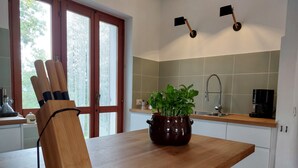 Une cuisine avec un plan de travail en bois, une plante en pot, une machine à café et une fenêtre avec des stores.