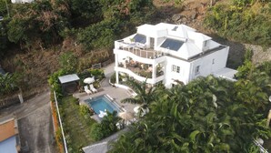 Ein mehrstöckiges Haus mit Pool, umgeben von üppiger Vegetation und einer hügeligen Landschaft.