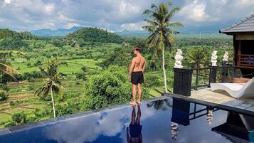 Un homme se tient au bord d’une piscine à débordement, d’où l’on peut admirer un paysage luxuriant et des montagnes en arrière-plan.