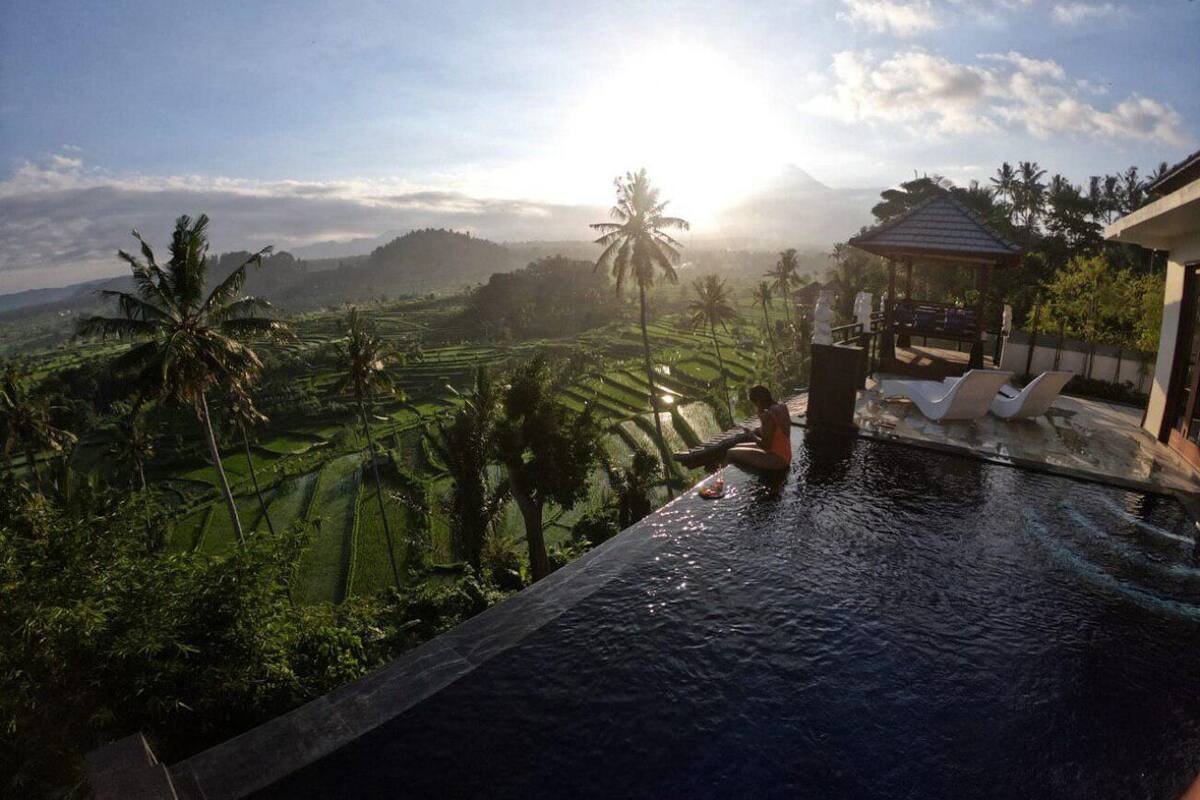 A pool with a view of terraced fields and palm trees, a gazebo, and lounge chairs.