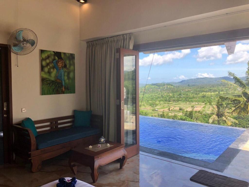 A room with a sofa, a fan, a painting, and a view of a pool and landscape.
